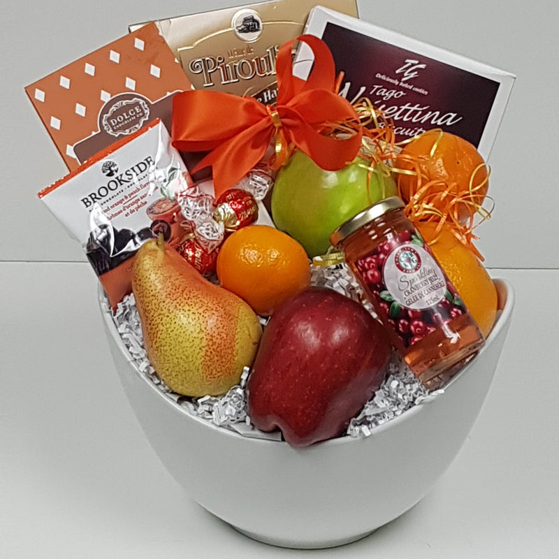 An assortment of fruit, delicious chocolates, cookies, sparkling jelly, and more is arranged in a ceramic bowl.