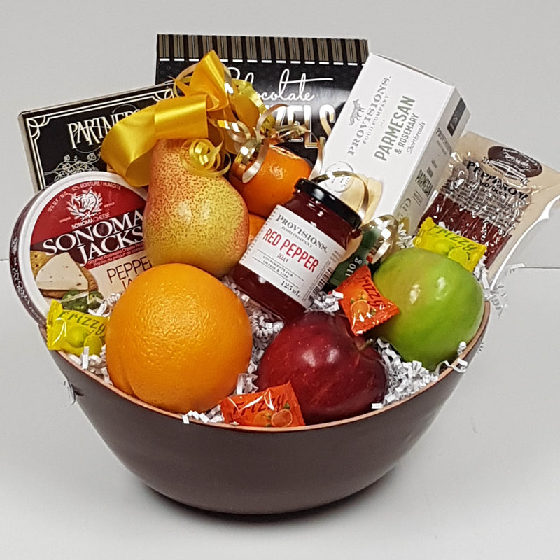 A bowl full of fruit, cheese and crackers, red pepper jelly, pepperoni and more.