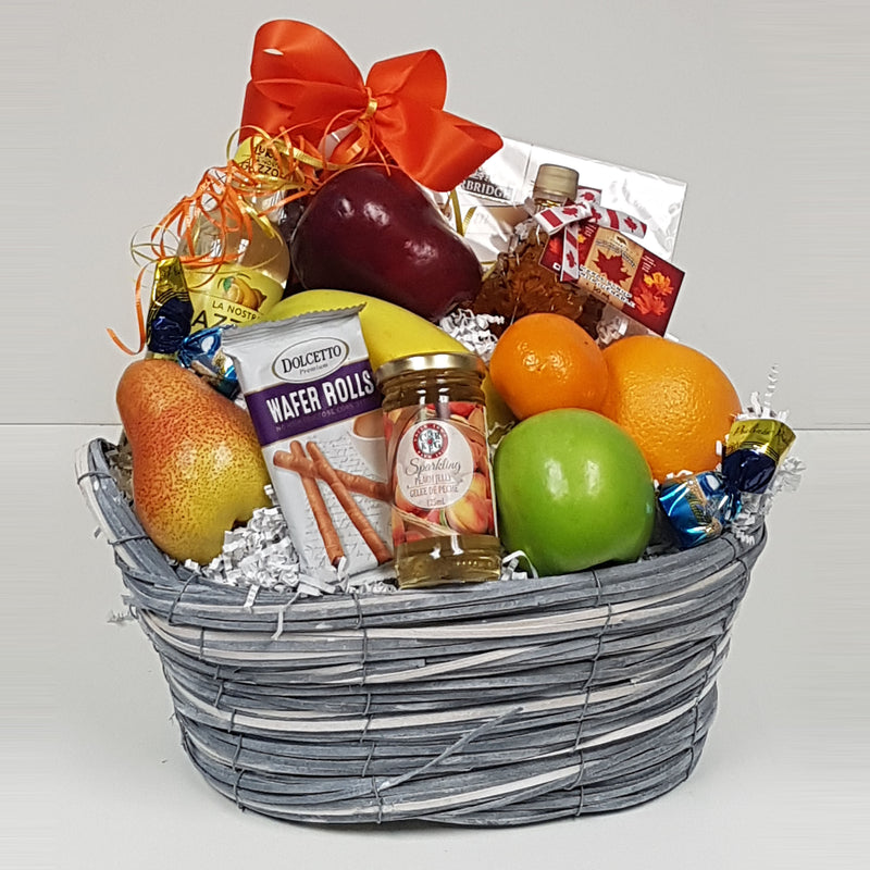 A basket of fruit, chocolate, biscuits, maple syrup, sparkling jelly and some sparkling water.