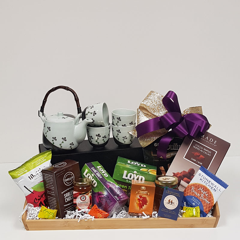 A wooden tray with a teapot and cups, a variety of teas, specialty honey, truffles, biscuits and shortbread, apple chips and sweets.