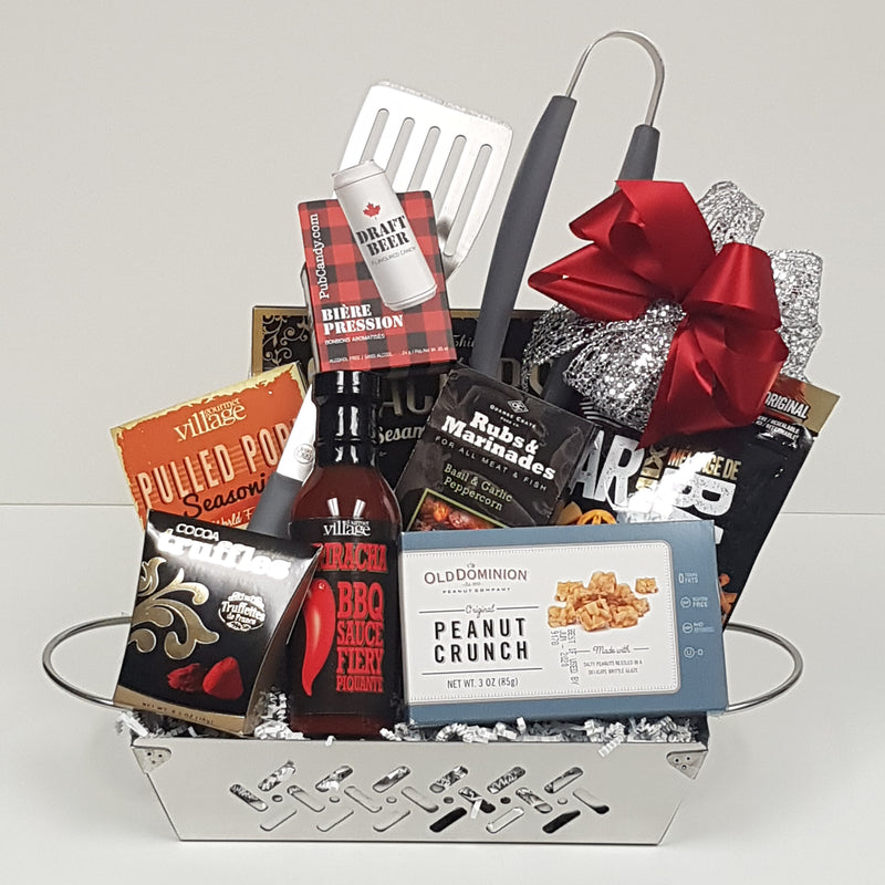 A stainless steel grill basket with a set of BBQ utensils, BBQ sauce and seasonings, bar mix munchies, truffles and peanut crunch.