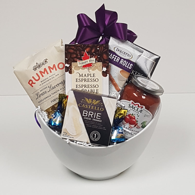 In a pasta bowl, there is Italian pasta and pasta sauce, crackers and brie, along with coffee, biscuits, and chocolate.