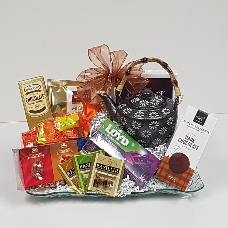 A glass tray with a classic teapot and a variety of tea and biscuits.
