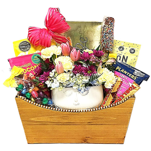 Easter Gift Basket with a pretty floral arrangement surrounded by delicious snacks and treats to enjoy. There's cookies, nut mix, chocolate, shortbread, biscuits, coconut drops and more. Lots of Easter treats!