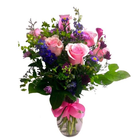 Vase arragnement of pink roses, field flowers and lush greenery with a pink bow. 
