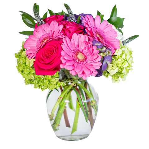 Vibrant pinks and greens make up this clear glass vase arrangement of roses, gerbera daisies and hydrangea.