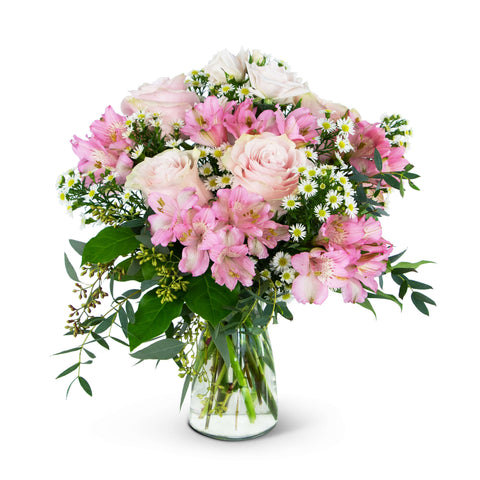 A clear glass vase filled with soft pink flowers. There's pink alstromeria and roses with white montes and lush greens. 