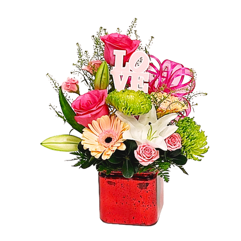 A cube vase with a floral arrangement of soft coloured florals.
