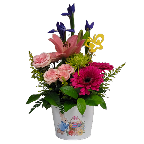 A tin pot is filled with gerbera daisies, irises, lilies and spray roses too.