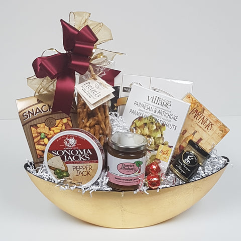 A bowl filled with chocolates, salty snack mix, pretzels, gourmet dip mix, crackers and cheese, chutney or antipasto, and mustard. 