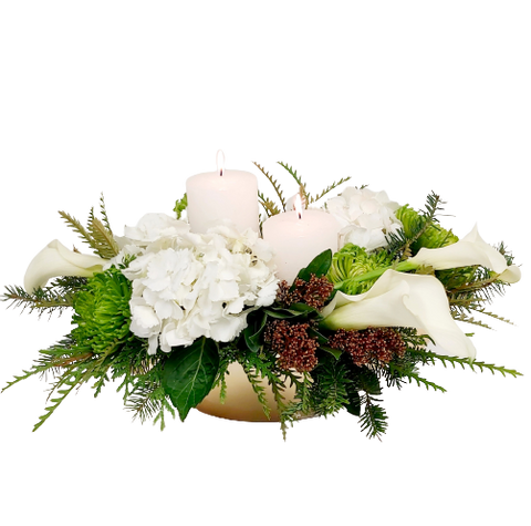 Two pillar candles amongst Christmas greens and blooms.