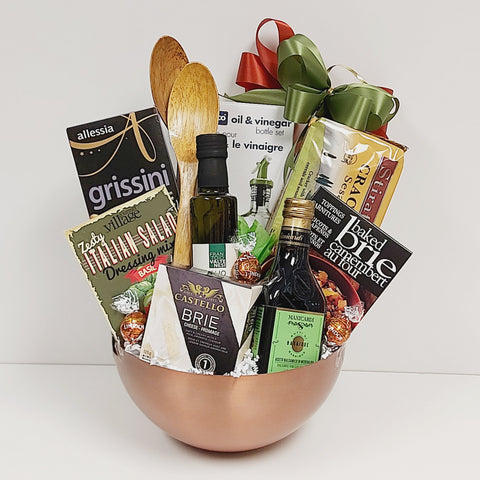 A copper-toned salad bowl filled with specialty oil and vinegar, a classy cruet set, salad dressing mix, crackers, cheese and cheese topping and handy salad spoons.